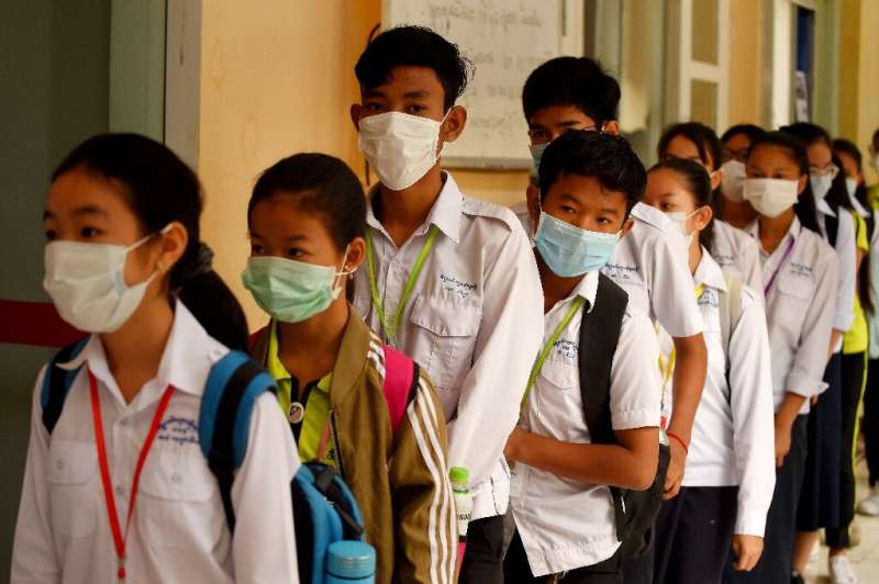 Masked Cambodian students line up to disinfect their hands with an alcohol solution before entering class at a school in Phnom P