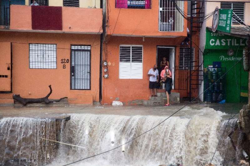 People look on as floodwaters from Storm Laura rips up streets in the Dominican Republic capital Santo Domingo