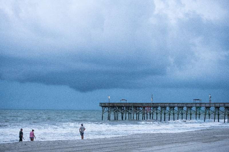 People walk along the beach in Myrtle Beach, South Carolina as Tropical Storm Isaias is set to strengthen into a hurricane and c