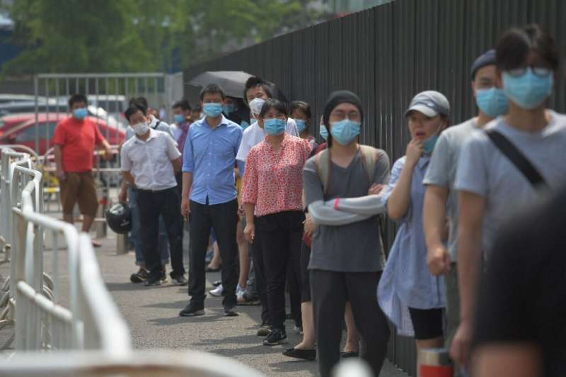 People wear masks as they wait in line to undergo COVID-19 swab tests at a testing station in Beijing
