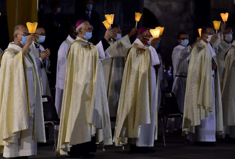 Prelates wearing face masks hold candles as they attend the 147th Assumption pilgrimage mass in France's Lourdes shrine on Augus