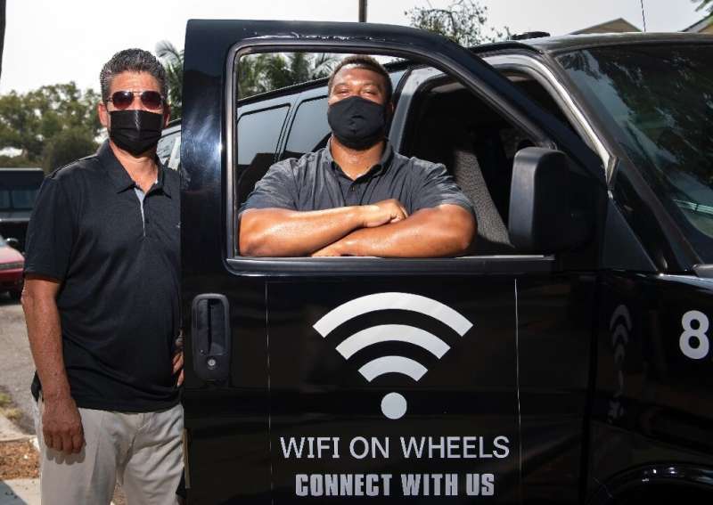 Roman Reyna (L) and Kevin Watson (R), of  JFK Transportation, pose by one of their minivans that give underserved kids wifi acce