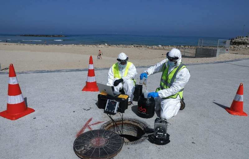 Technicians from Israeli firm Kando extract sewage samples from a manhole near the beach, in the southern coastal Israeli city o
