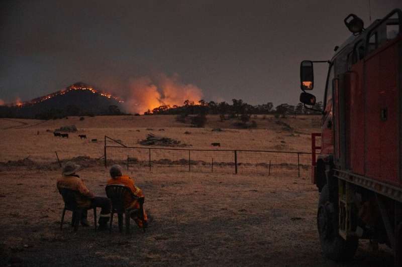 Volunteer firefighters watch as a bushfire rages on the outskirts of the town of Tumbarumba in New South Wales