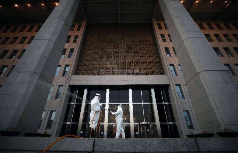 Workers spray disinfectant outside the National Assembly in Seoul, as the number of coronavirus infections continued to rise