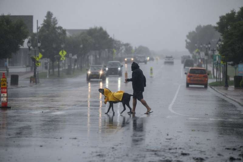 A man and dog walk cross a street before traffic as Tropical Storm Henri approaches, in Montauk, Long Island on August 22, 2021