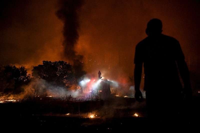 A person watches a fire fighter dousing flames from the top of a truck as a fire spreads around the village of Afidnes, some 30 