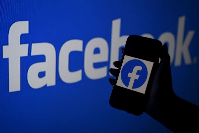 A smart phone screen displays the logo of Facebook on a Facebook website background