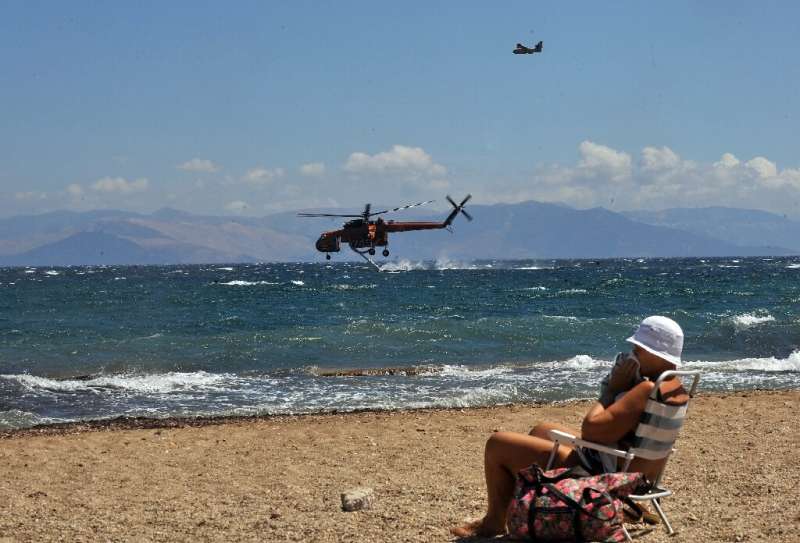 A woman sits on the beach while firefighting planes fill up with water in a resort of Nea Makri in eastern Athens on August 24, 