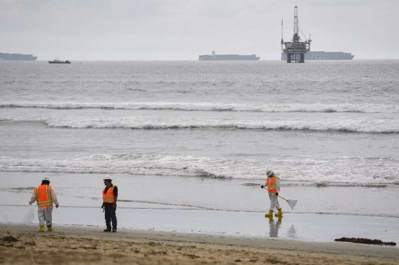 An oil platform and cargo container ships are seen on the horizon as environmental response crews clean the beach after an oil s