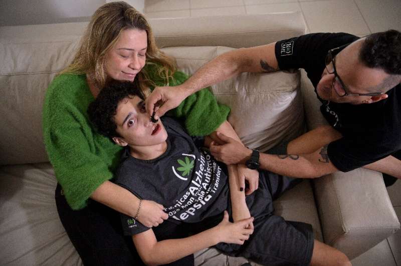 Gabriel Guerra (C) is held by his mother, Vanessa Opitz, while his father Ricardo Guerra gives him medicinal cannabis in Rio de 