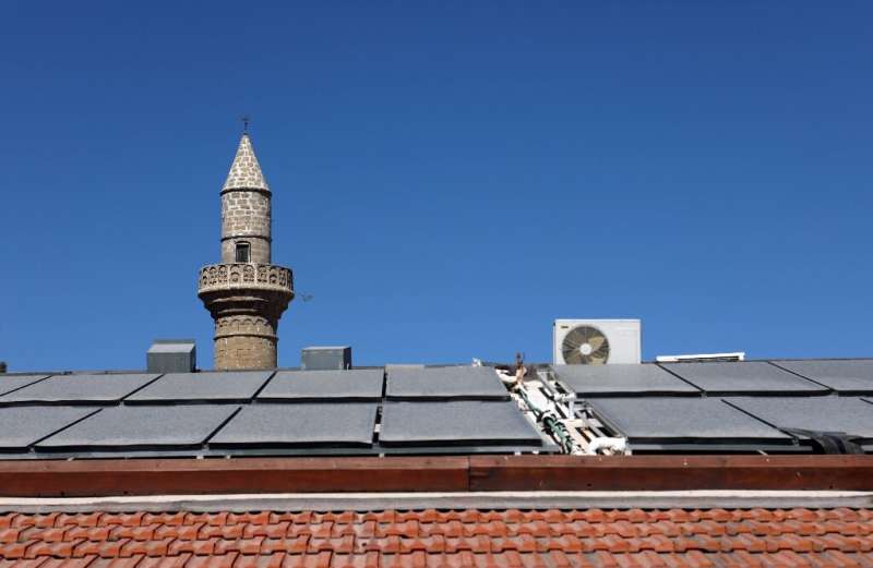 Solar panels cover the roof of a house in the village of Kalavasos, in front of a mosque minaret, but Cyprus is still struggling