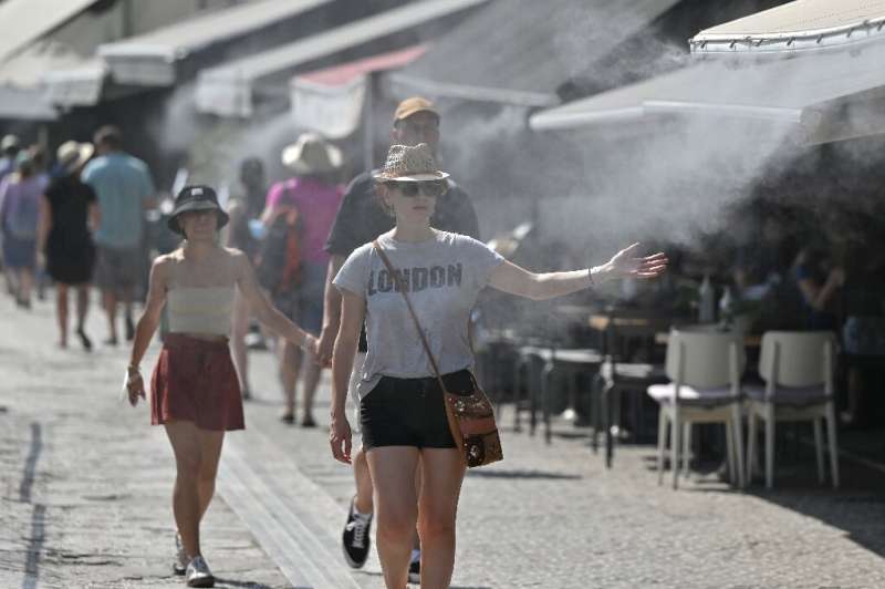 Tourists walk through water sprayed by a mister at a cafe during a heatwave in Athens