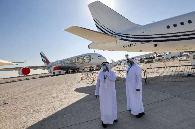 Two men stand next to an Acropolis Aviation Airbus A320-251N aircraft, with an Emirates Airbus A380 aircraft in the background, 