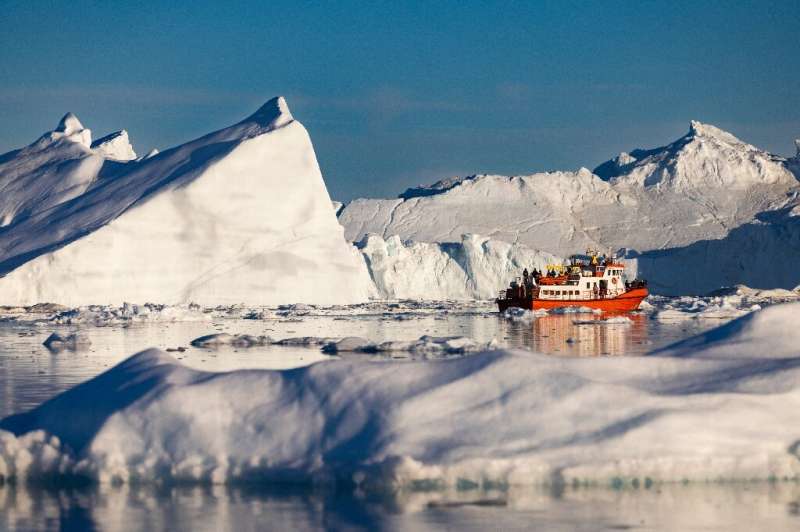 A boat carrying tourists weaves through icebergs floating in Disko Bay, Ilulissat, western Greenland