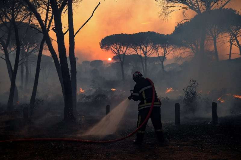 Un bombero francés utiliza una manguera de agua, ya que la luz del sol poniente se filtra a través del humo durante un incendio forestal, cerca de G