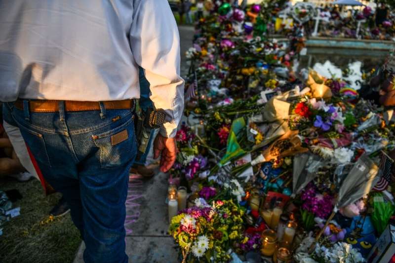 A man carries a gun as he visits a memorial for the shooting victims outside the Uvalde County Courthouse in Uvalde, Texas on Ma