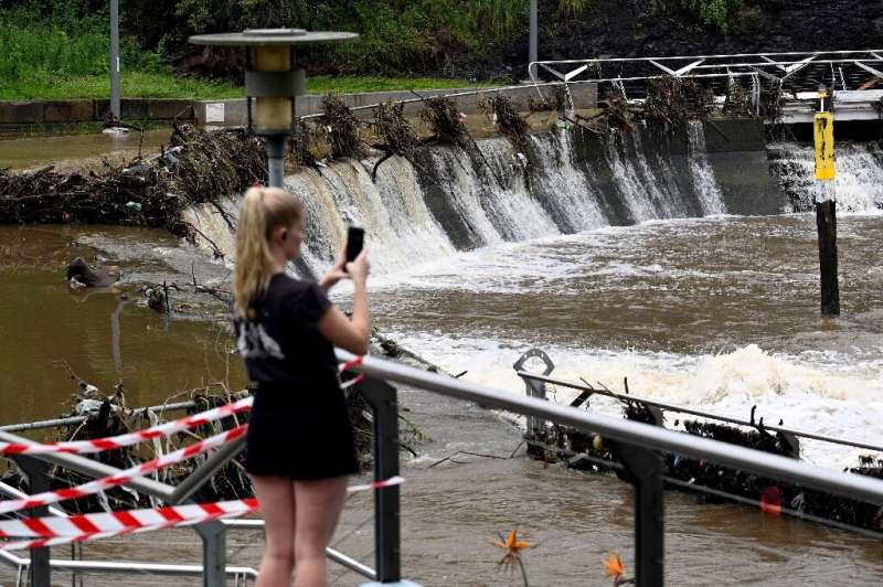 A woman takes pictures of the overflowing Parramatta river at the ferry wharf in Sydney