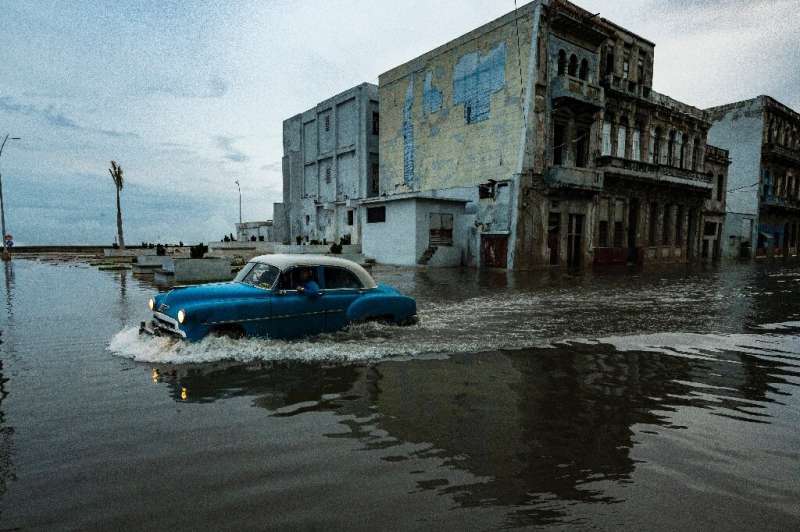 An old American car passes through a street left flooded by Hurricane Ian in Havana