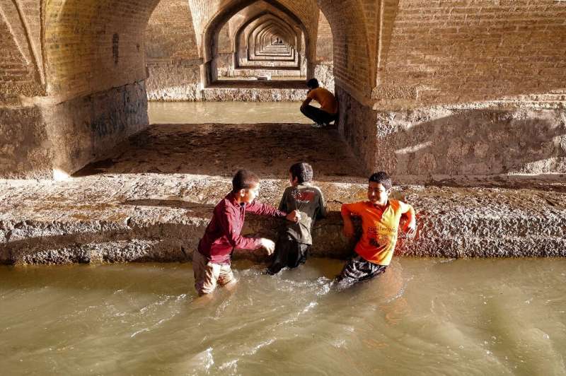 Boys wade in the water of the Zayandeh Rood beneath the arches of the Si-o-Se Pol bridge