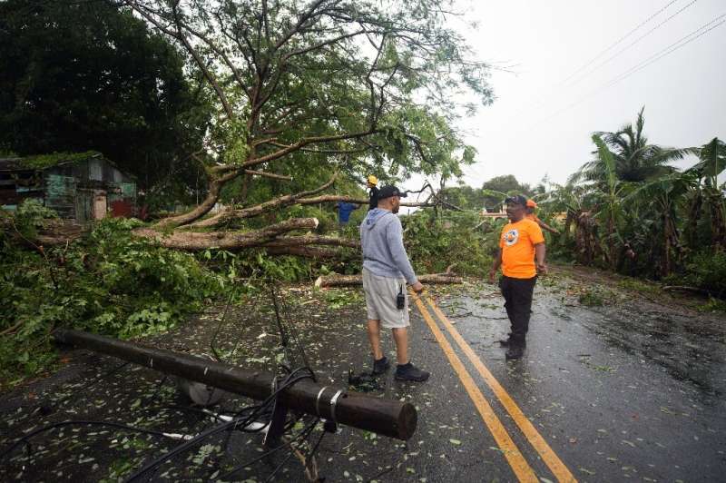Civil defense personnel and firefighters remove fallen trees from a highway in the Dominican Republic