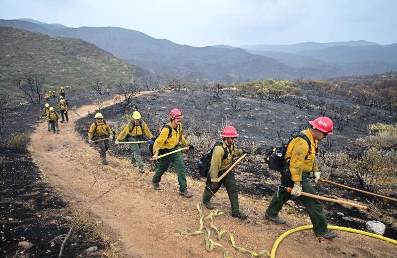 Firefighters walk past a scorched landscape from the Fairview fire inside the San Bernardino National Forest near Hemet, Califor