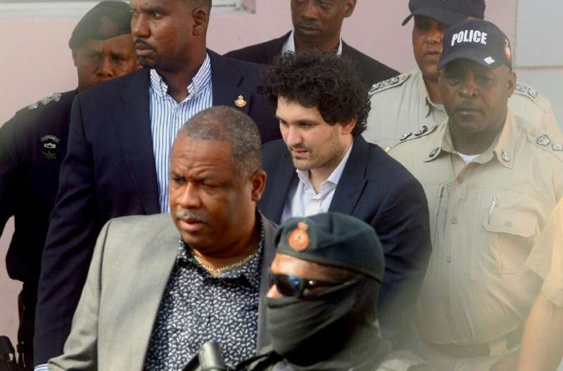 FTX founder Sam Bankman-Fried (C) is led away handcuffed from a Nassau, Bahamas court by law enforcement officials after a heari