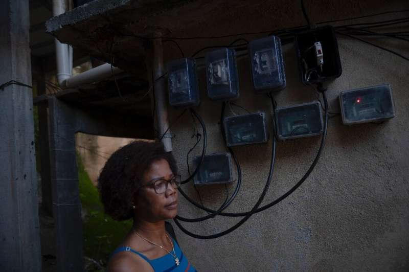 Marcia Campos, one of the participants in Babilonia favela's solar co-op, stands next to the power meter on her home