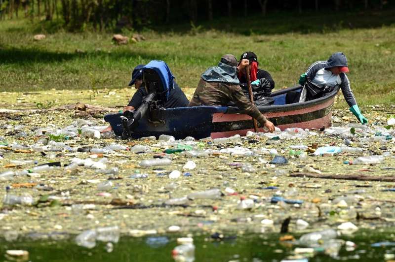 People in a boat clean up plastic rubbish from the Cerron Grande in Potonico, El Salvador by hand