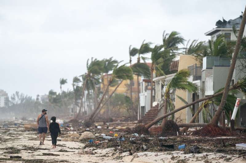 People walk along the beach looking at property damaged by Hurricane in Ian Bonita Springs, Florida