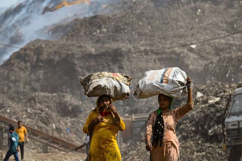 Ragpickers carrying sacks walk near the Bhalaswa landfill in New Delhi on April 28, 2022, after a fire broke out there
