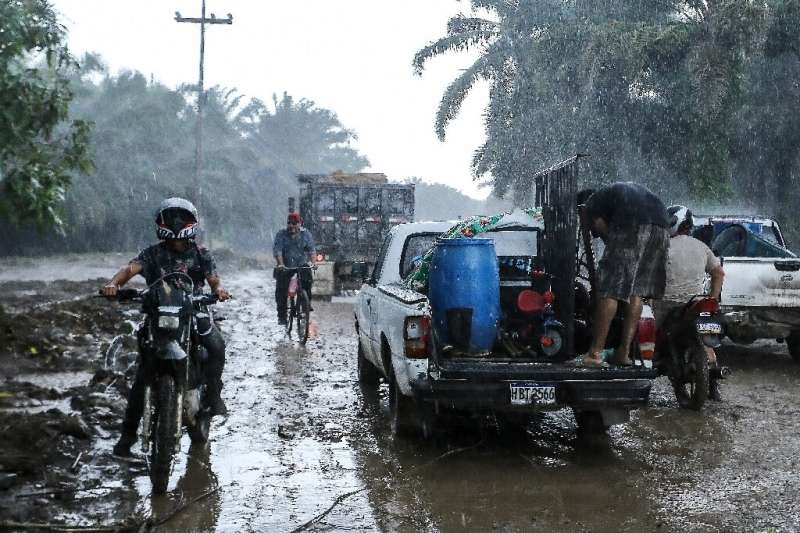 Residents leave their homes in the municipality of El Progreso, Honduras under pouring rain on October 8, 2022, before the arriv
