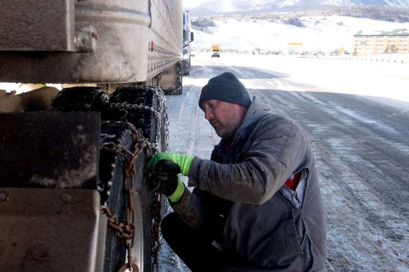 Robert Arnold of Denver, Colorado puts chains onto the tires of his semitrailer while he waits for the eastbound lane of I-70 to