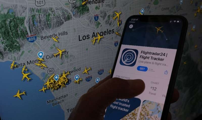 The Flightradar24 app is seen on a smartphone in front of a screen showing the live position of planes tracked by the app in the