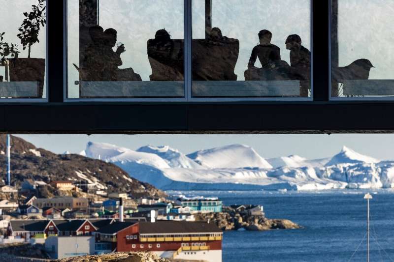 Tourists enjoy a drink as they sit on a viewing bridge overlooking icebergs floating in Disko Bay, Ilulissat, western Greenland