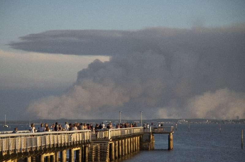 Tourists watch dark smoke from the pier in Andernos-les-Bains, France due to a wildfire near La Teste in the southwest of the co