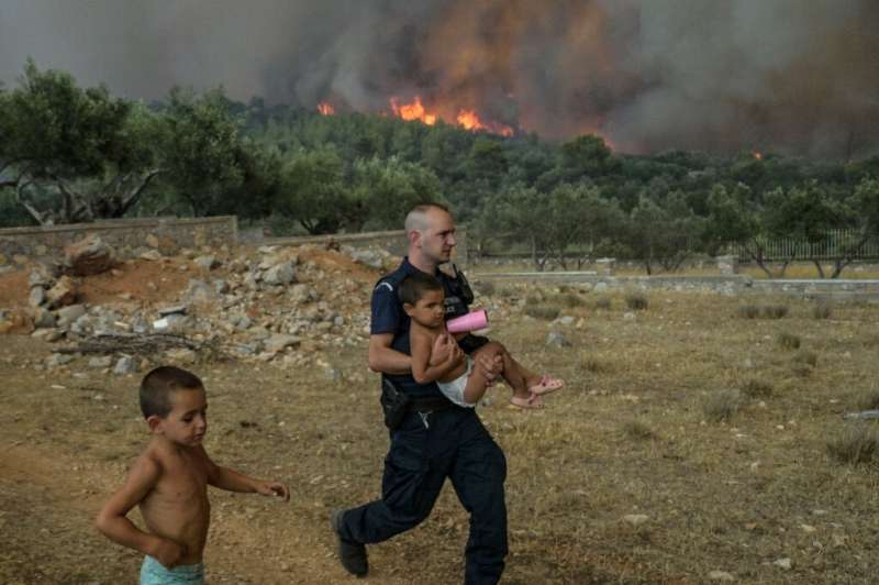 A Greek police officer evacuates a child from a wildfire at the village of Agios Charamlabos, near Athens