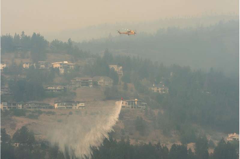 A helicopter drops water as the McDougall Creek wildfire continues to burn in West Kelowna, British Columbia