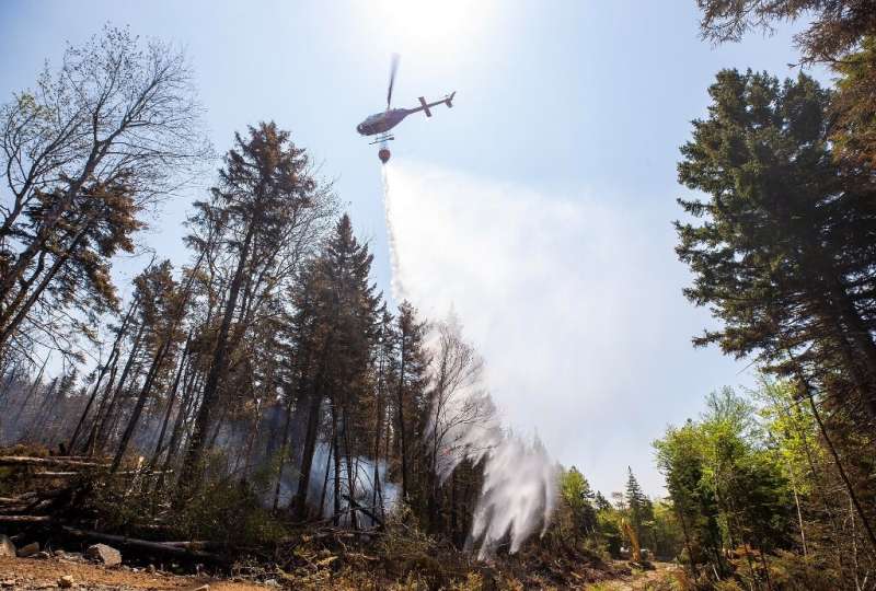 A helicopter drops water on a hotspot as an excavator makes a fire break at Canada's Tantallon wildfire on June 1, 2023