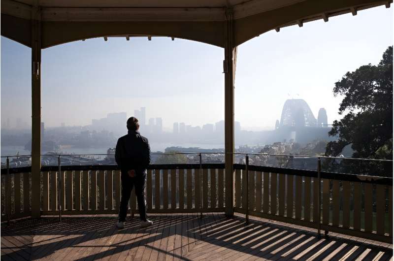 A man looks out from his balcony at the Sydney skyline on September 13, 2023, as smoke blankets Sydney Harbour after a ring of c