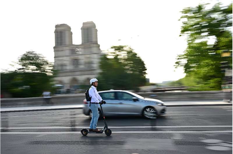 A man rides an electric scooter or trottinette past the Notre-Dame de Paris Cathedral