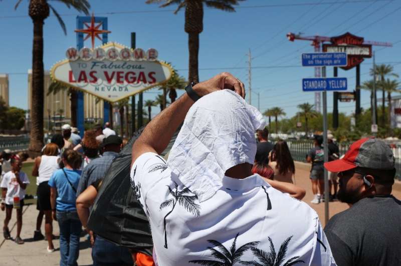 A man shields himself from the sun while waiting in line to take a photo at the historic 'Welcome to Las Vegas' sign during a he