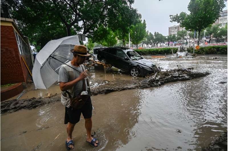A man stands near a damaged car after heavy rains in Mentougou district in Beijing