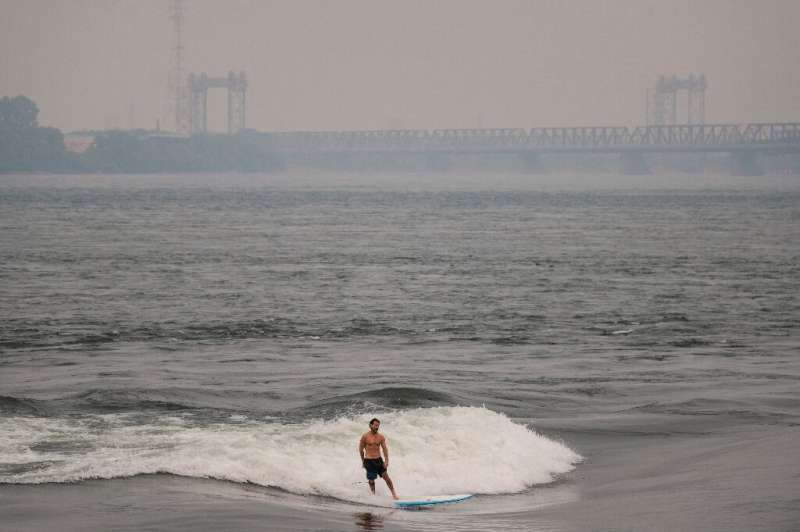 A man surfs in the St. Lawrence river with smoke caused by wildfires in northern Quebec in the background in Montreal, Canada on