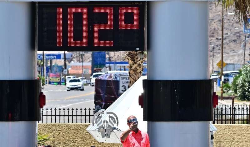 A man takes a selfie in front of a thermometer showing the temperature at 102F (38.9C) in southern California