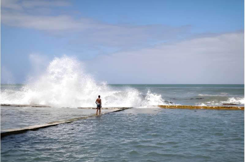 A man walks on a sea wall as waves spray water on Kalk Bay in Cape Town