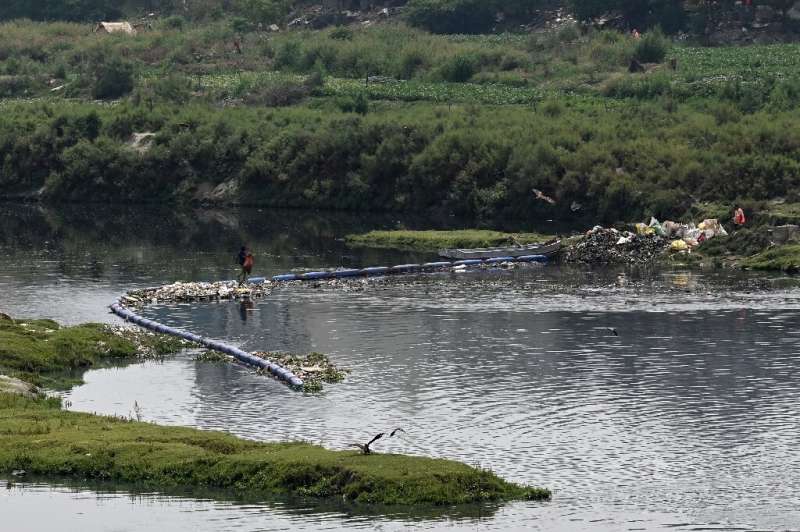 A man walks over a floating barrier stopping waste from a sewage canal leading to New Delhi's Yamuna River, one of the filthiest