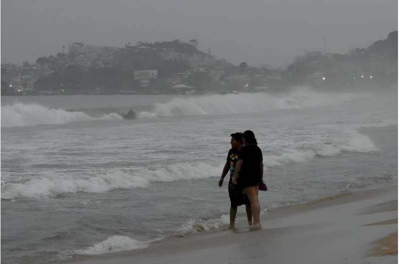 Beach-goers look out to sea as Hurricane Otis approaches the Mexican tourist resort of Acapulco