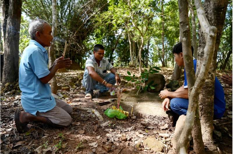 Eam Orn (L) kneels in a Cambodian forest, pressing his hands together before an offering, and prays for the return of his land