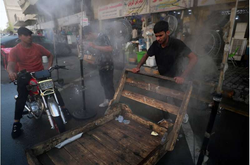 Men cool off with a mist dispenser set up in a street in central Baghdad amid soaring temperatures